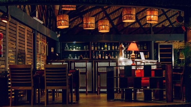 Zona de bar con muebles de madera, lámparas colgantes y una variedad de botellas.