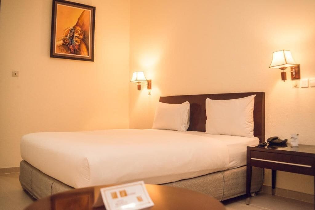 A hotel room with a large bed, two bedside lamps, a nightstand, and a painting on the wall.