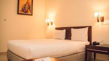 A hotel room with a large bed, two bedside lamps, a nightstand, and a painting on the wall.