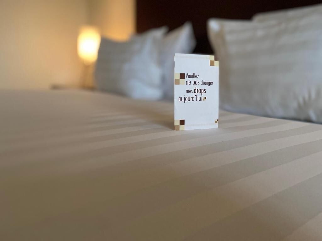 A bed with white linens and pillows, a bedside lamp, and a small white object with text on it.