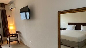 Una habitación de hotel con cama, televisión montada en la pared, una silla y una lámpara.