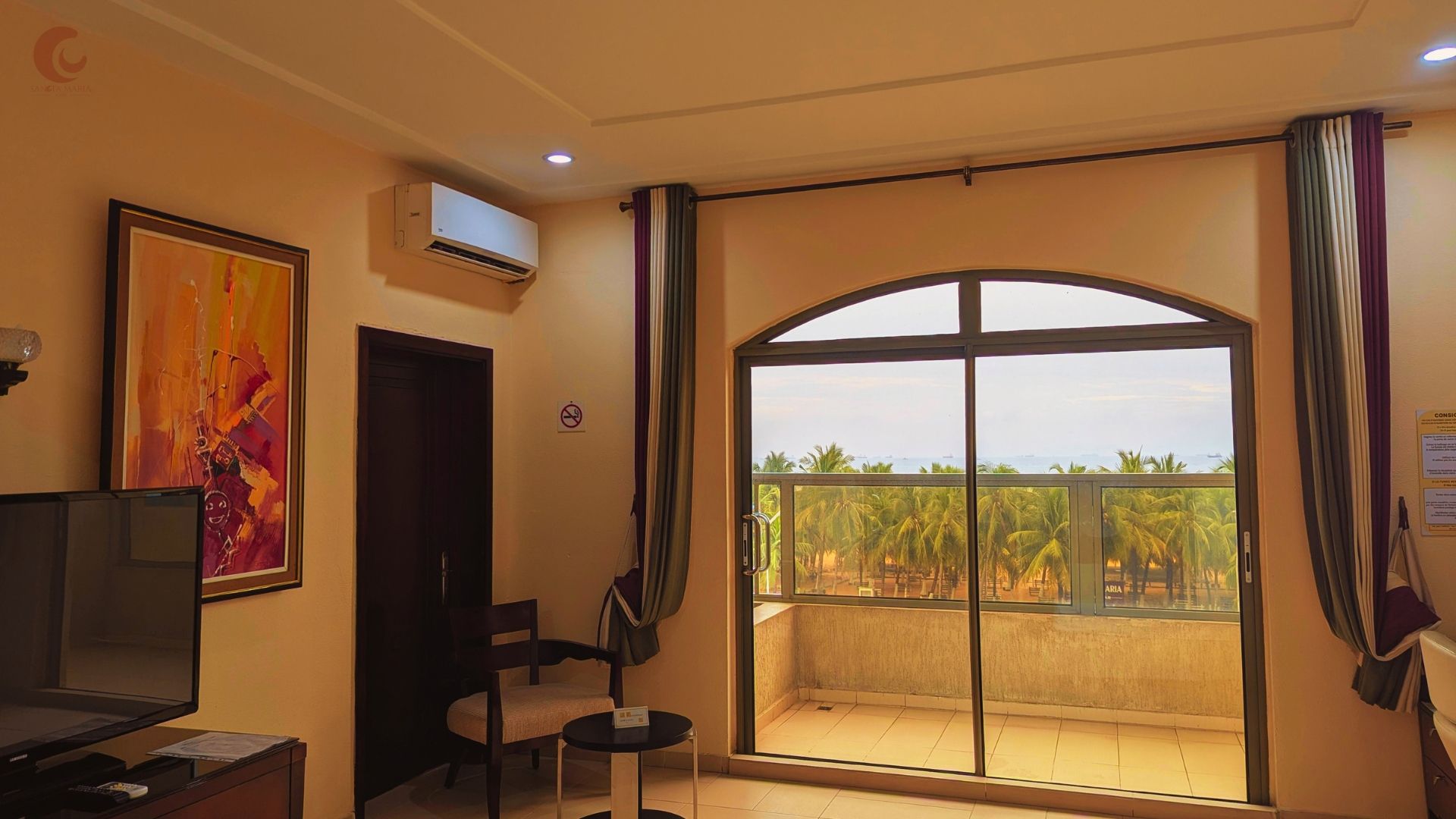 A hotel room with a balcony, a television, a painting, and a no-smoking sign.