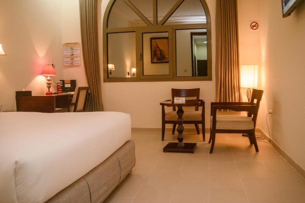 A hotel room with a bed, a desk, a chair, and a window with curtains.