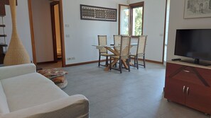 A living room with a sofa, a dining table with chairs, a television, and a cabinet.