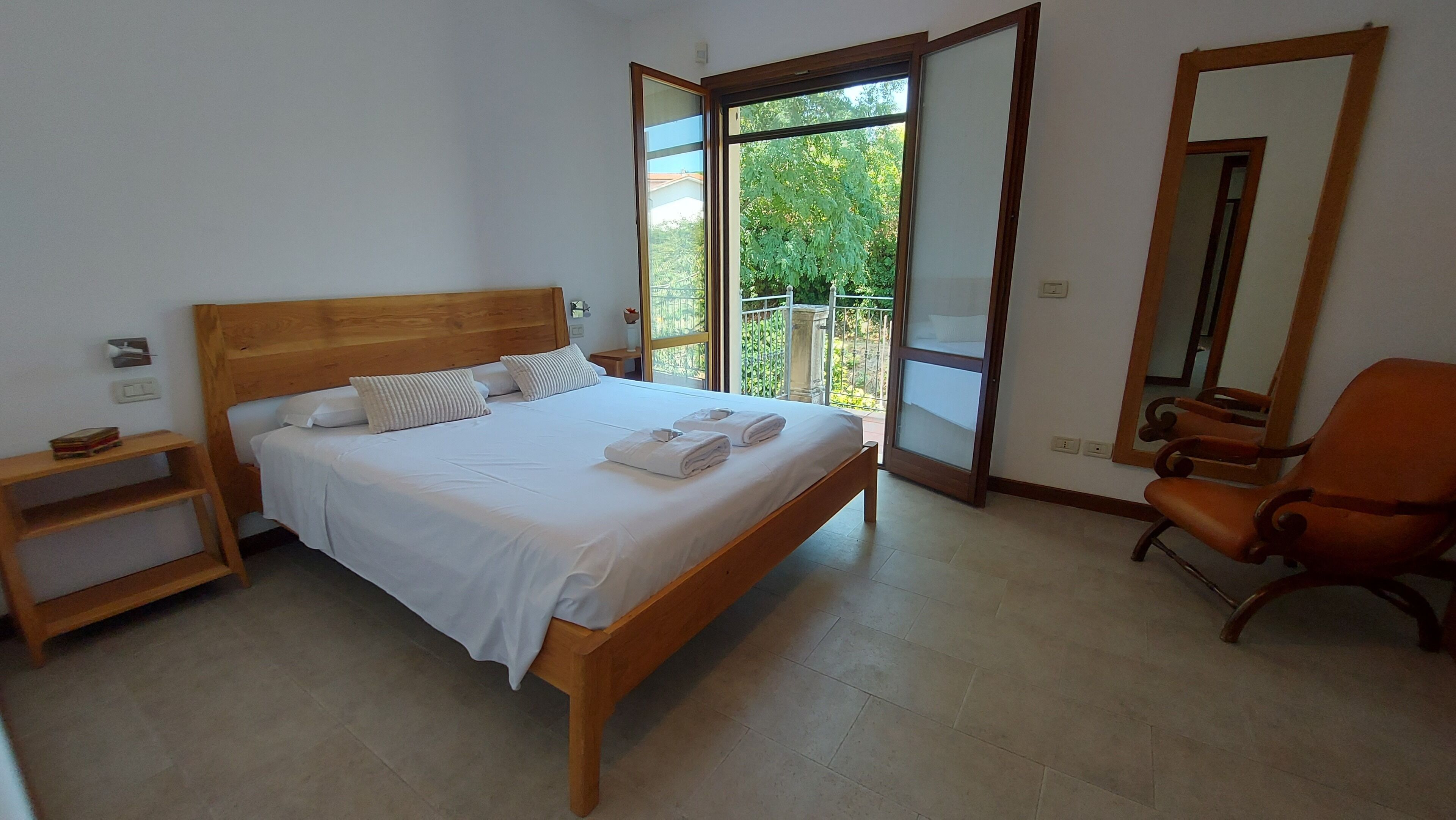 Une chambre à coucher avec un lit en bois, une table de chevet, une chaise et une grande fenêtre donnant sur un paysage verdoyant.