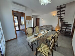 A dining area with a glass table, striped chairs, a sofa, and a wooden staircase.