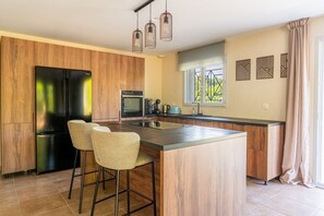 Eine moderne Küche mit einer zentralen Kochinsel, Barhocker, einem Kühlschrank und Pendelleuchten.