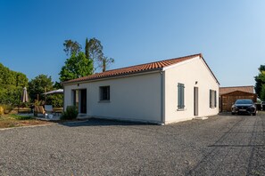 A single-story building with a tiled roof, a gravel driveway, and a parked car. - L'air du Médoc - Jolie maison pour 6 avec jardin (Cussac-Fort-Médoc)