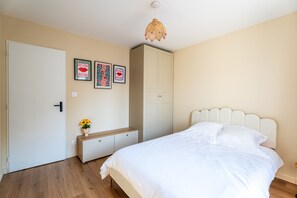 A bedroom with a bed, a wardrobe, a bench, and wall art. - L'air du Médoc - Jolie maison pour 6 avec jardin (Cussac-Fort-Médoc)