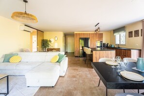 Ein modernes Wohnzimmer mit Sofa, Esstisch und Küchenzeile, inklusive Kühlschrank und Kaffeemaschine.