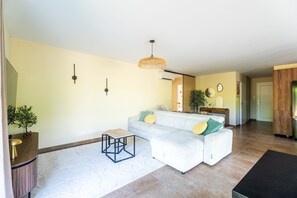 A modern living room with a sectional sofa, a small coffee table, and a hanging light fixture. - L'air du Médoc - Jolie maison pour 6 avec jardin (Cussac-Fort-Médoc)