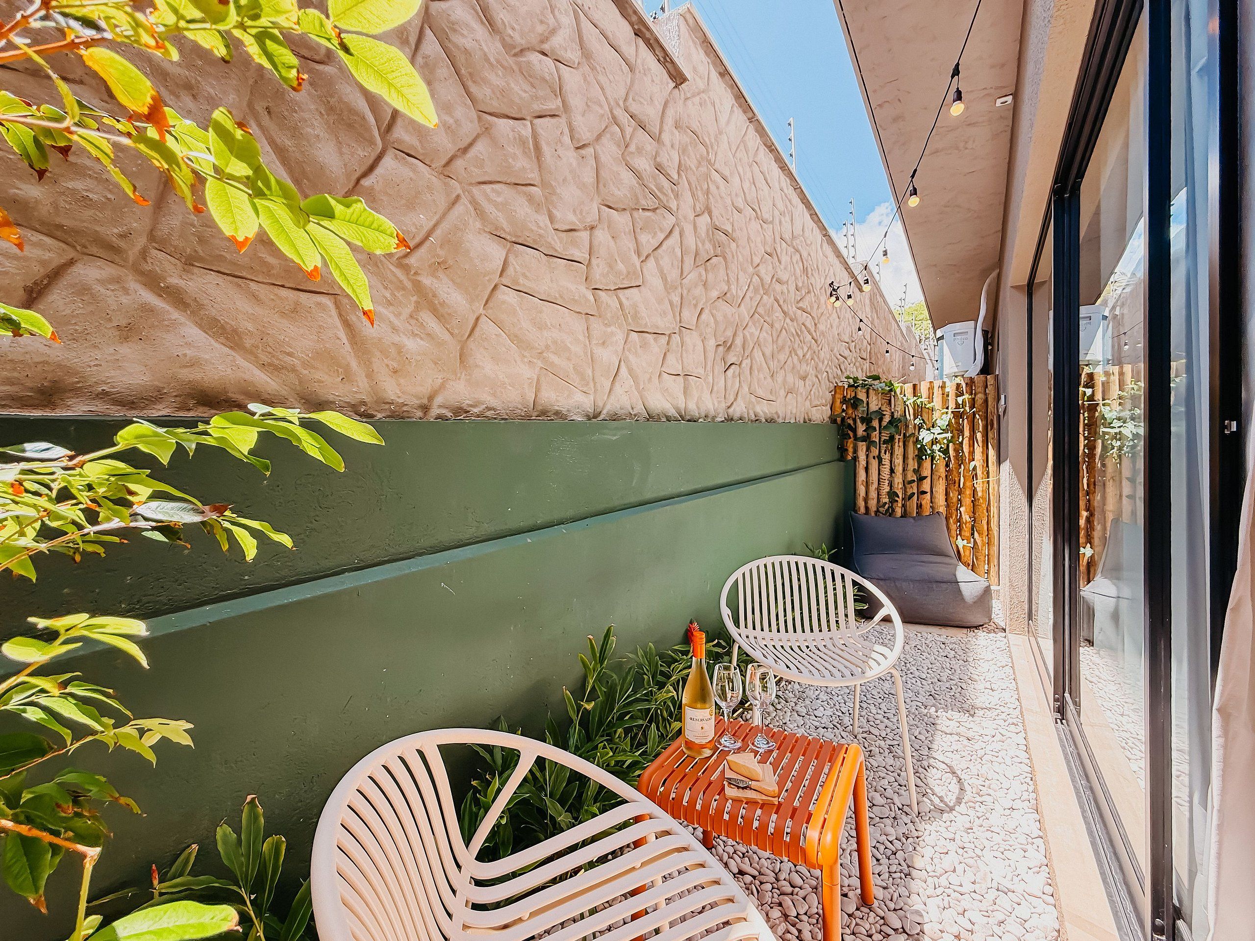 A patio area with a stone wall, a green painted wall, and a seating arrangement with two chairs and a table.