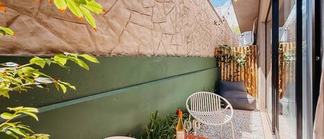 A patio area with a stone wall, a green painted wall, and a seating arrangement with two chairs and a table.