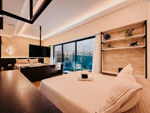A modern hotel room with a large bed, a desk, a flat-screen TV, and a view of the outdoors. - Mondrian - Ponta Negra by Almare Flats (Natal)