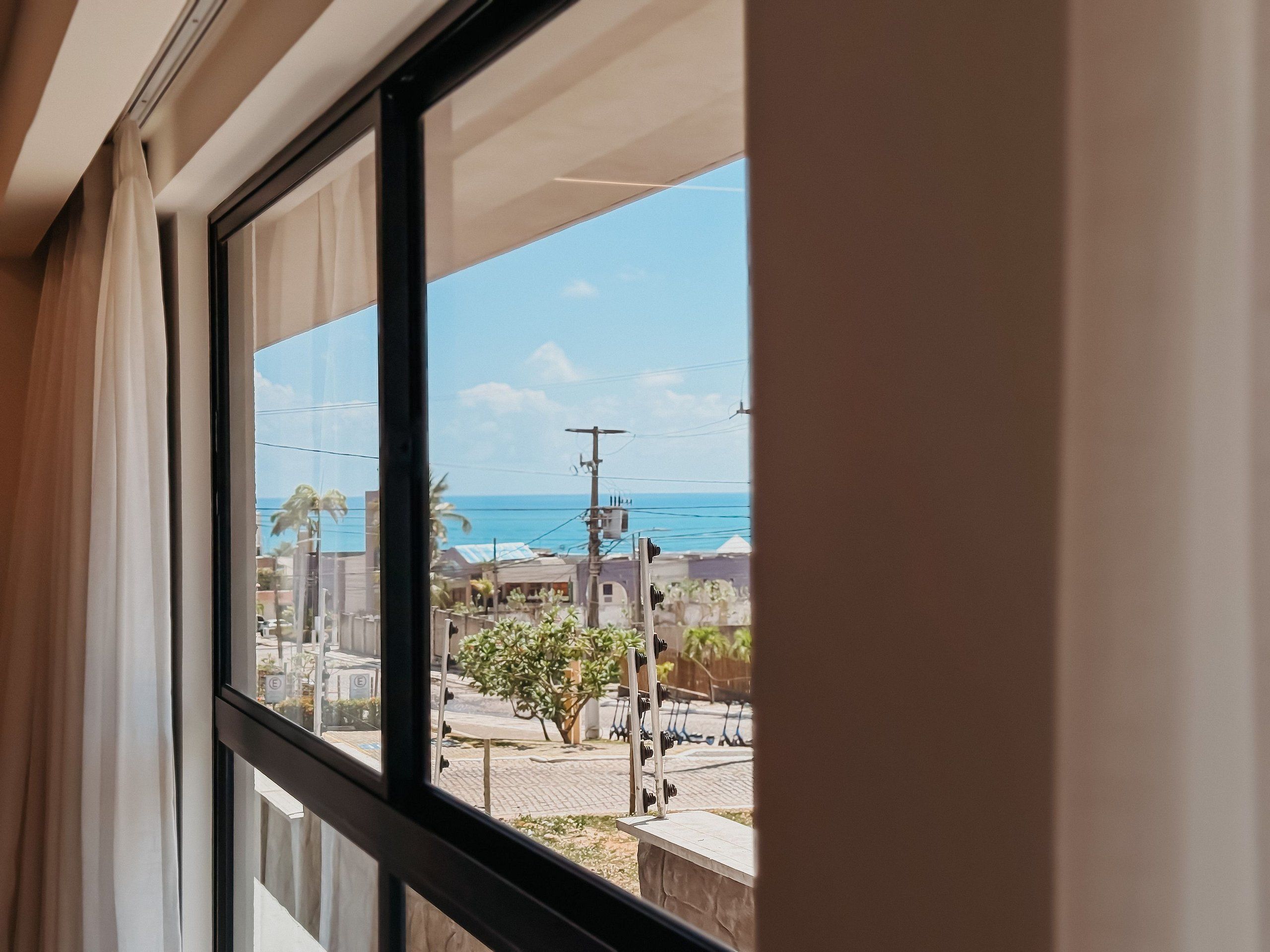A window with a view of a street and buildings, a clear sky, and a distant body of water.