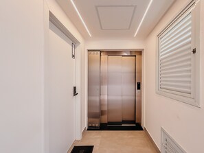 Un ascensor moderno con revestimiento metálico, una puerta con placa de número y una rejilla en la pared.