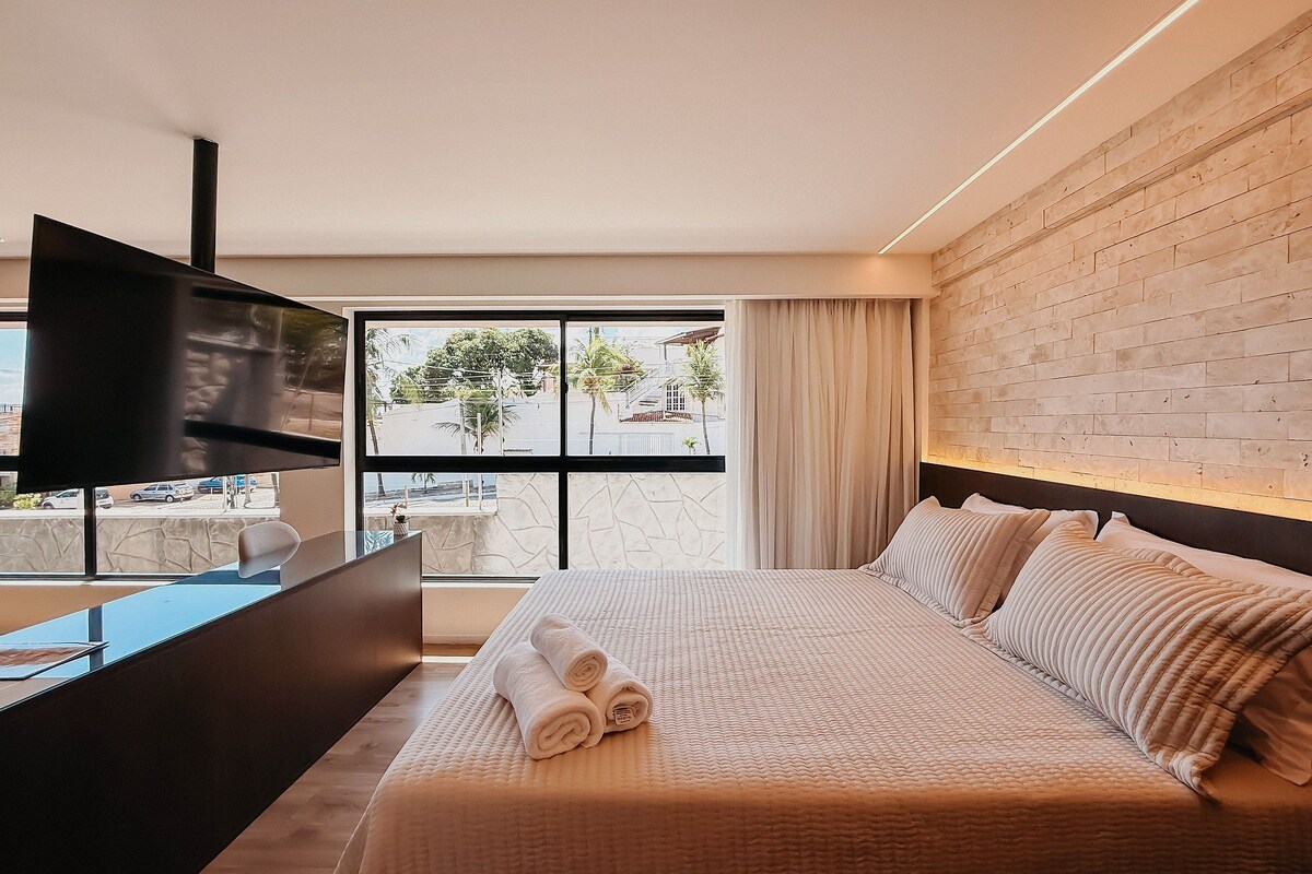 A modern hotel room with a large bed, a flat-screen TV, and a view of the street through a large window.