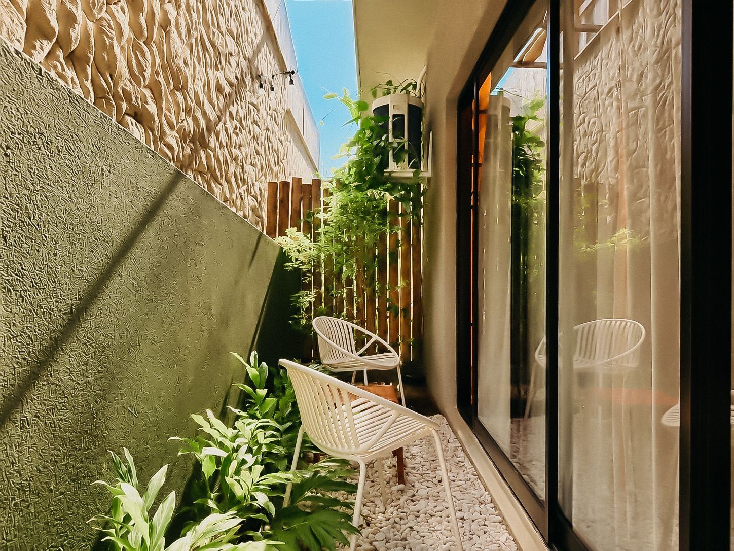 Un petit espace extérieur avec un mur à texture, deux chaises blanches et des plantes en pot.