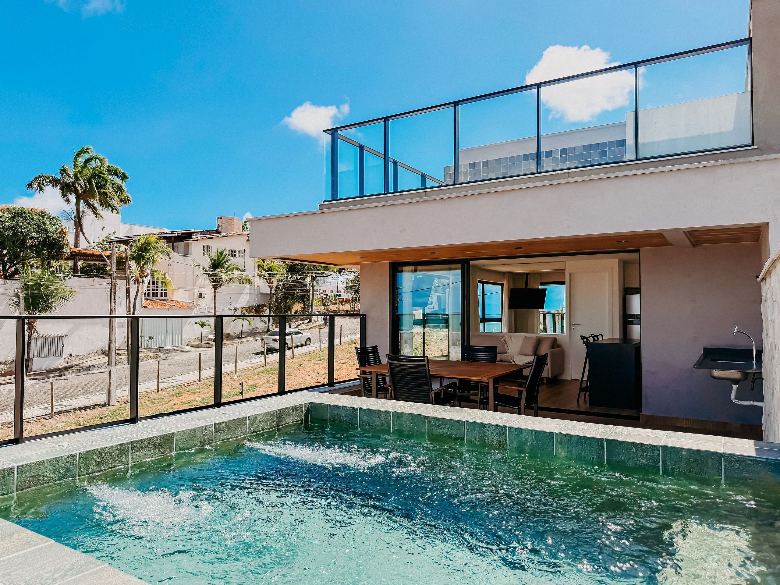 A modern two-story building with a swimming pool, outdoor seating, and a view of the street.