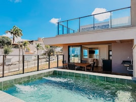Un edificio moderno de dos pisos con piscina, asientos exteriores y vista a la calle.