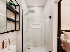 A modern bathroom with a glass-enclosed shower, a toilet, and a shelf with decorative items. - Mondrian - Ponta Negra by Almare Flats (Natal)