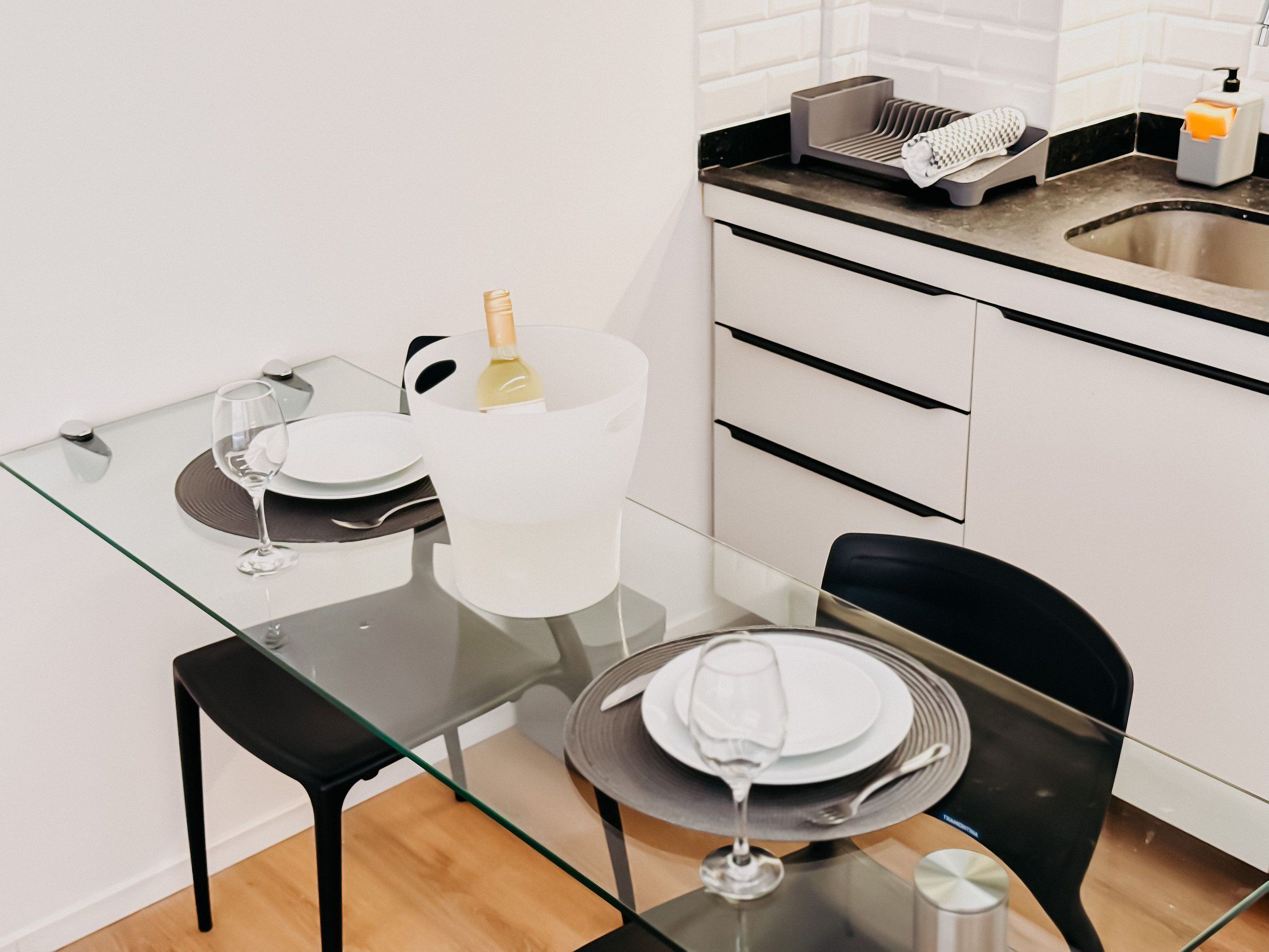 A modern kitchen with a glass dining table, black chairs, and a wine glass.