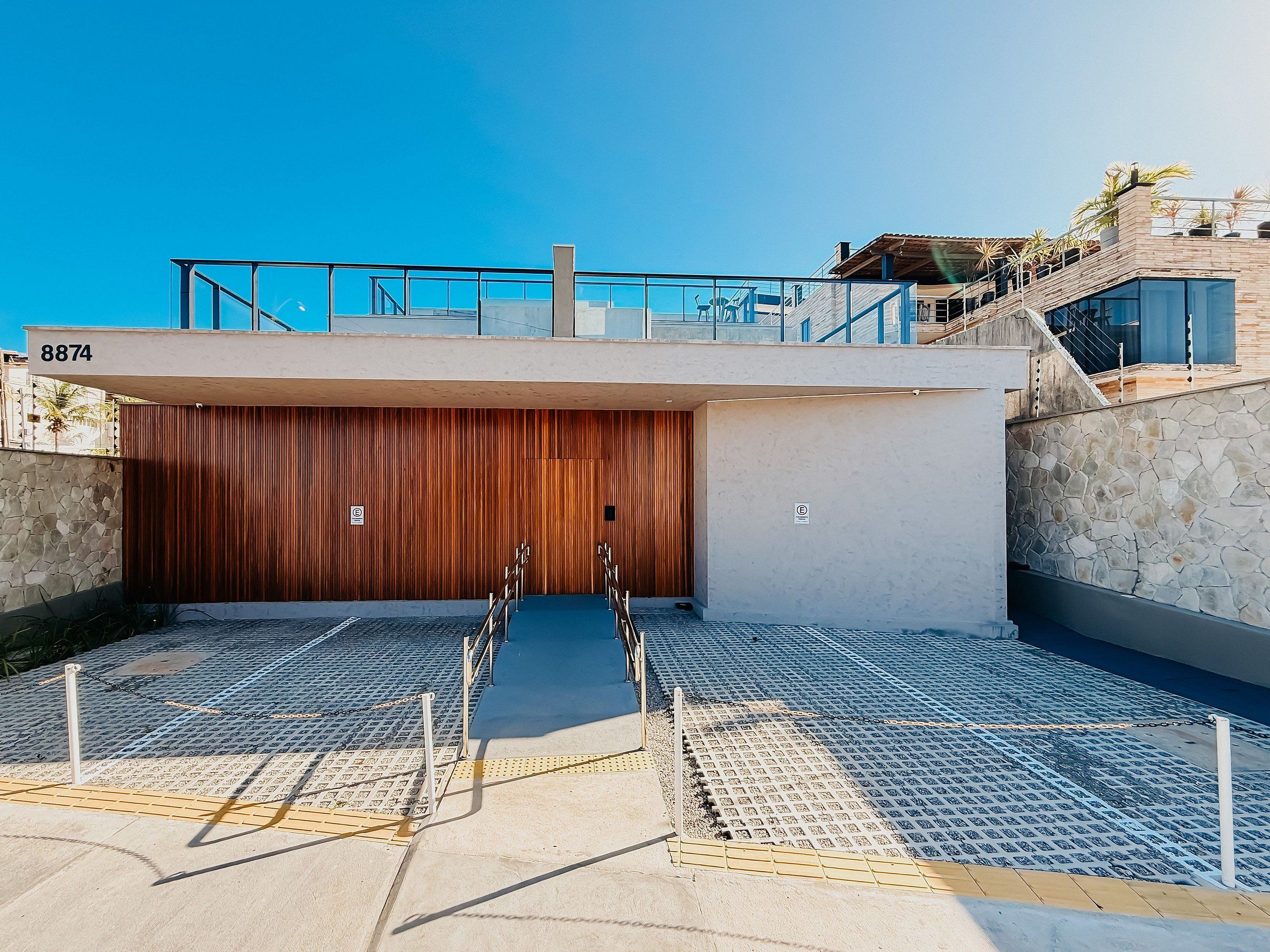 A modern building with a large wooden door, a balcony with railings, and a stone wall.