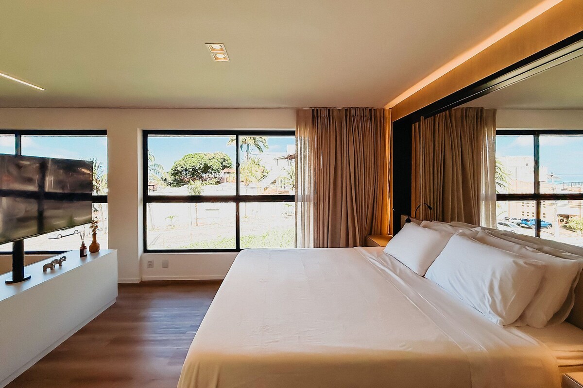 A hotel room with a large bed, a flat-screen TV, a window with a view of the outdoors, and a ceiling light.