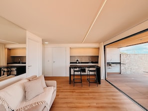 A modern kitchen with a dining area, a sofa, and a view of the outdoors.