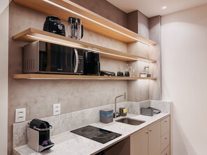 A modern kitchen with a built-in microwave, coffee maker, and a kettle on the countertop. - Mondrian - Ponta Negra by Almare Flats (Natal)