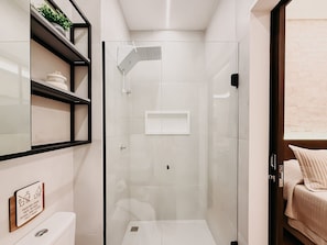 A modern bathroom with a glass-enclosed shower, a toilet, and a shelf with decorative items. - Mondrian - Ponta Negra by Almare Flats (Natal)