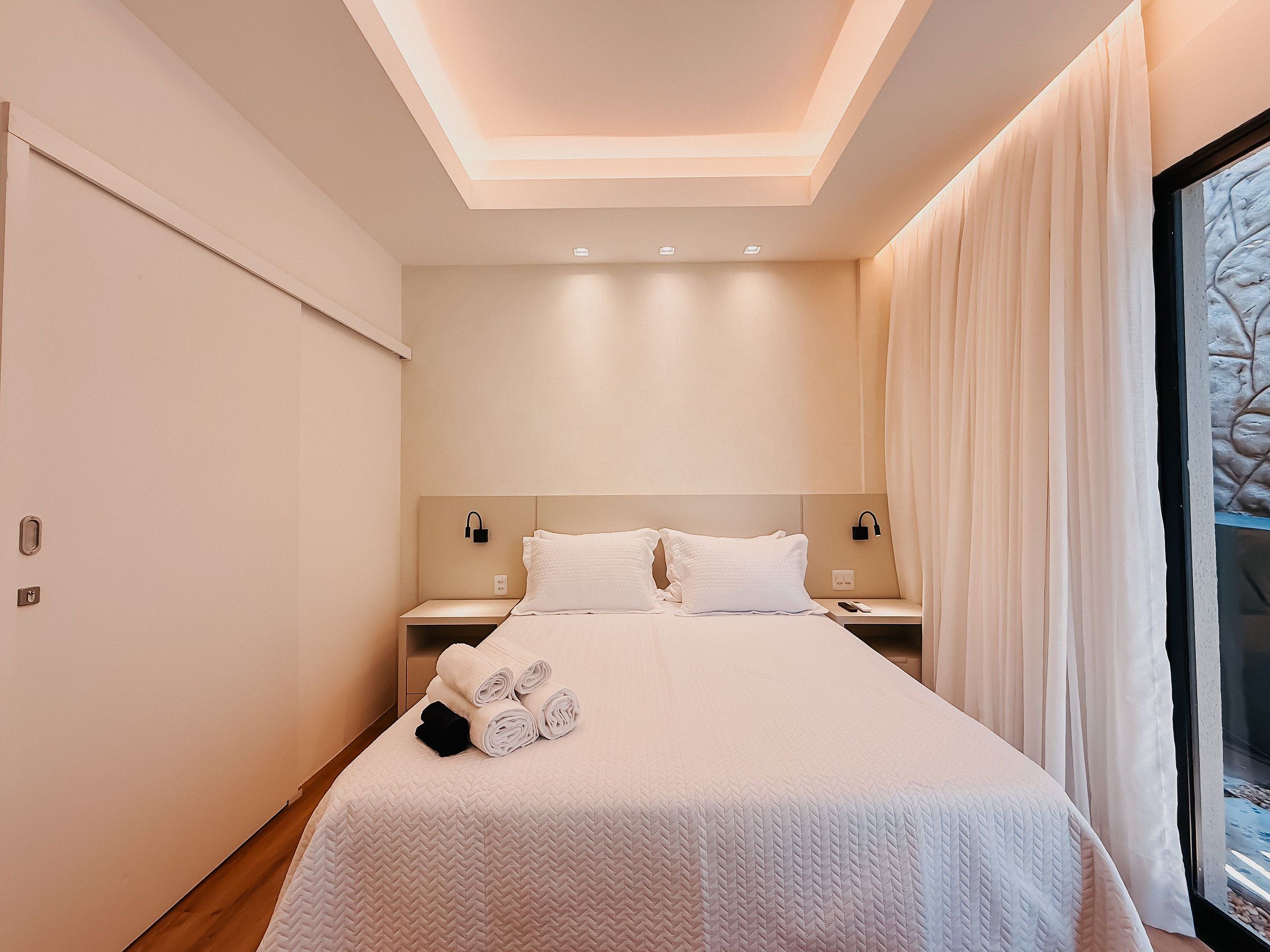 A modern hotel room with a large bed, a nightstand, and a window with curtains.