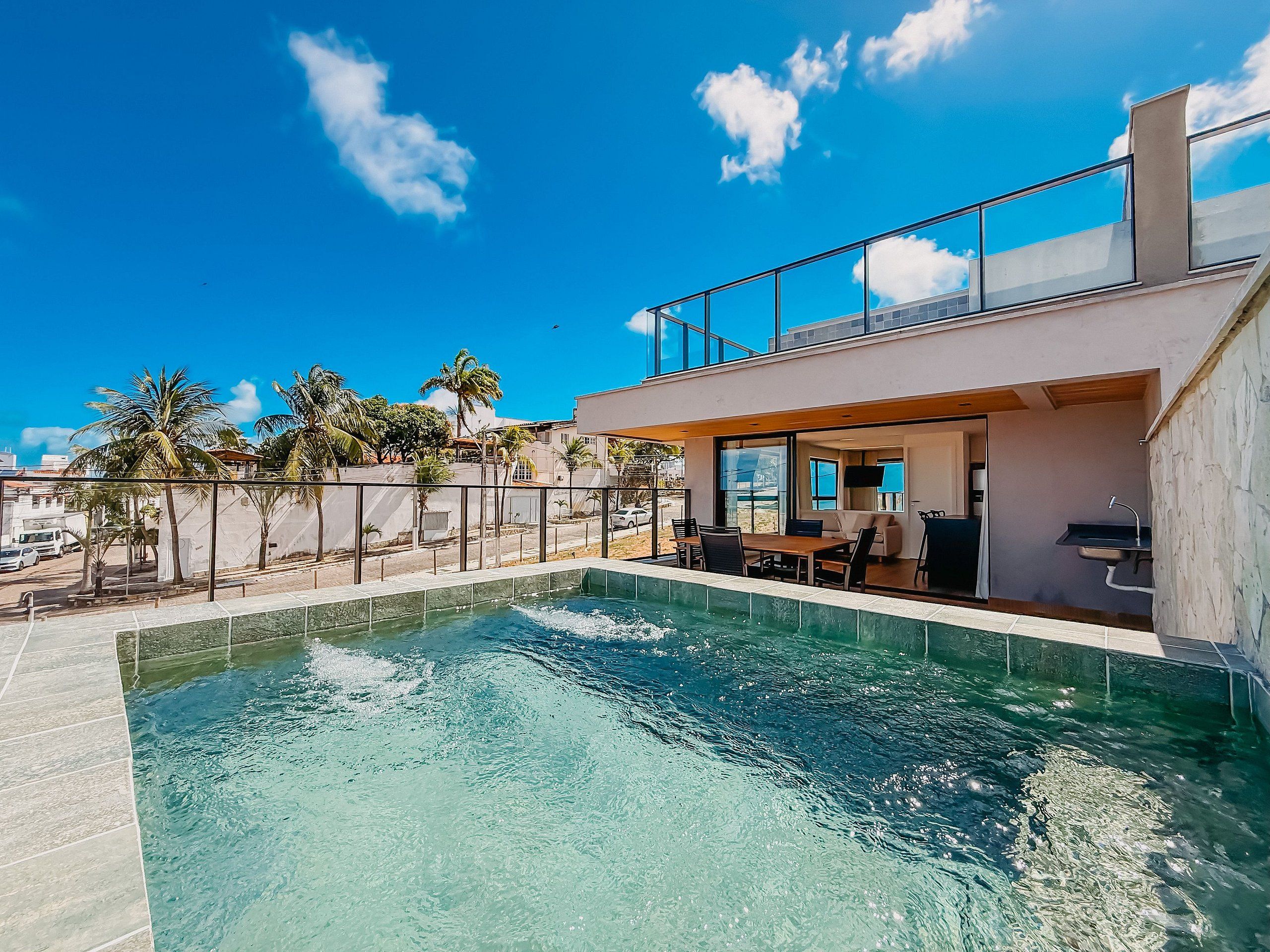 A modern pool area with a clear blue pool, a covered seating area, and a view of the surrounding landscape.