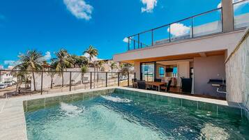 A modern pool area with a clear blue pool, a covered seating area, and a view of the surrounding landscape.