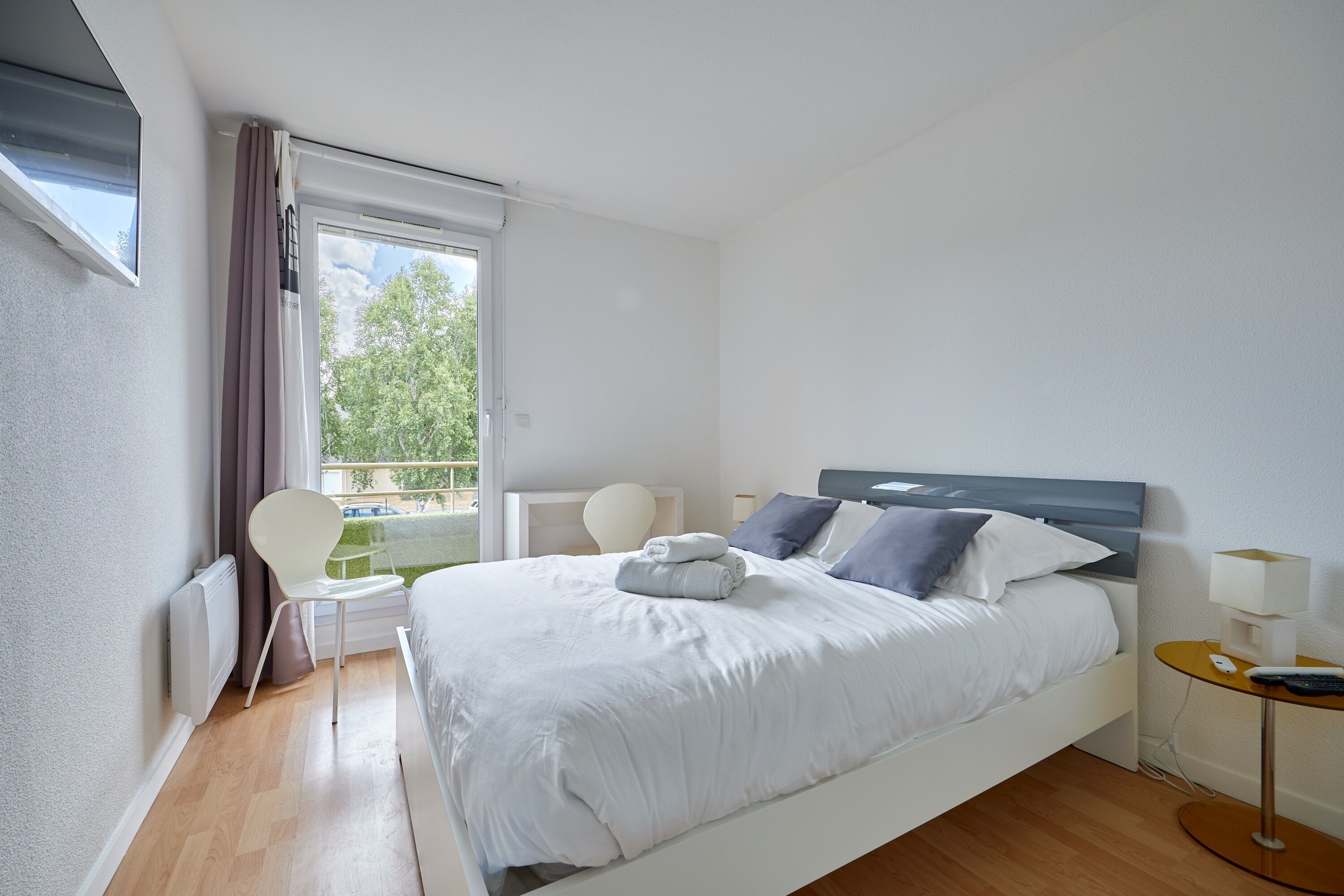 Una camera da letto moderna con un letto, comodini, una sedia e vista sul verde.