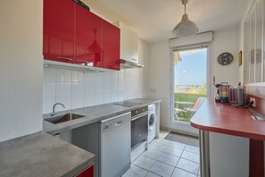 A compact kitchen with a washing machine, a sink, and a red cabinet. - Évasion Côte Fleurie - Proche Plage (Touques)