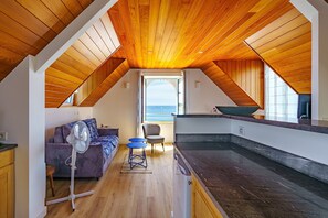 Ein kompakter Wohnraum mit schrägverdeckter Decke, einer Couch, einem kleinen Tisch und Meerblick.