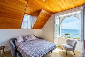 A bedroom with a bed, a chair, and a large window with a view of the sea. - Le Puits d'Amour - Joli appt pour 3 avec vue mer (Benodet)