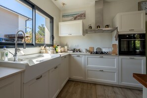 A modern kitchen with white cabinetry, a built-in oven, and a window overlooking a street. - Les Hirondelles du Lac - Avec piscine privée (La Teste-de-Buch)