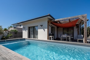Ein modernes Haus mit Swimmingpool, einer überdachten Terrasse mit Sitzgelegenheit und einem umzäunten Garten.