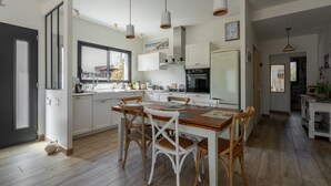 Una cocina moderna con armarios blancos, una mesa de comedor con sillas e iluminación colgante.