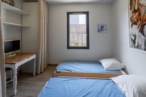 Ein Schlafzimmer mit zwei Einzelbetten, einem Schreibtisch mit Computer, einem Fenster und einem Bild an der Wand.