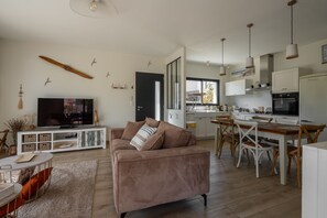 A modern living room with a sofa, television, and a dining area with chairs and a table. - Les Hirondelles du Lac - Avec piscine privée (La Teste-de-Buch)