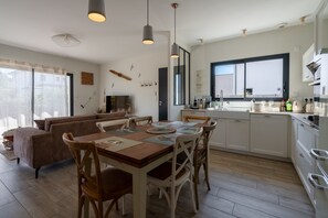 A modern kitchen with a dining area, wooden flooring, and a large window. - Les Hirondelles du Lac - Avec piscine privée (La Teste-de-Buch)