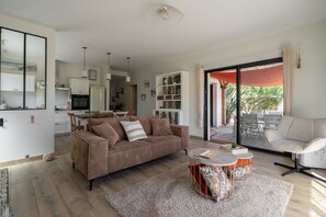 A modern living room with a brown sofa, a coffee table, and a view of the outdoor patio. - Les Hirondelles du Lac - Avec piscine privée (La Teste-de-Buch)