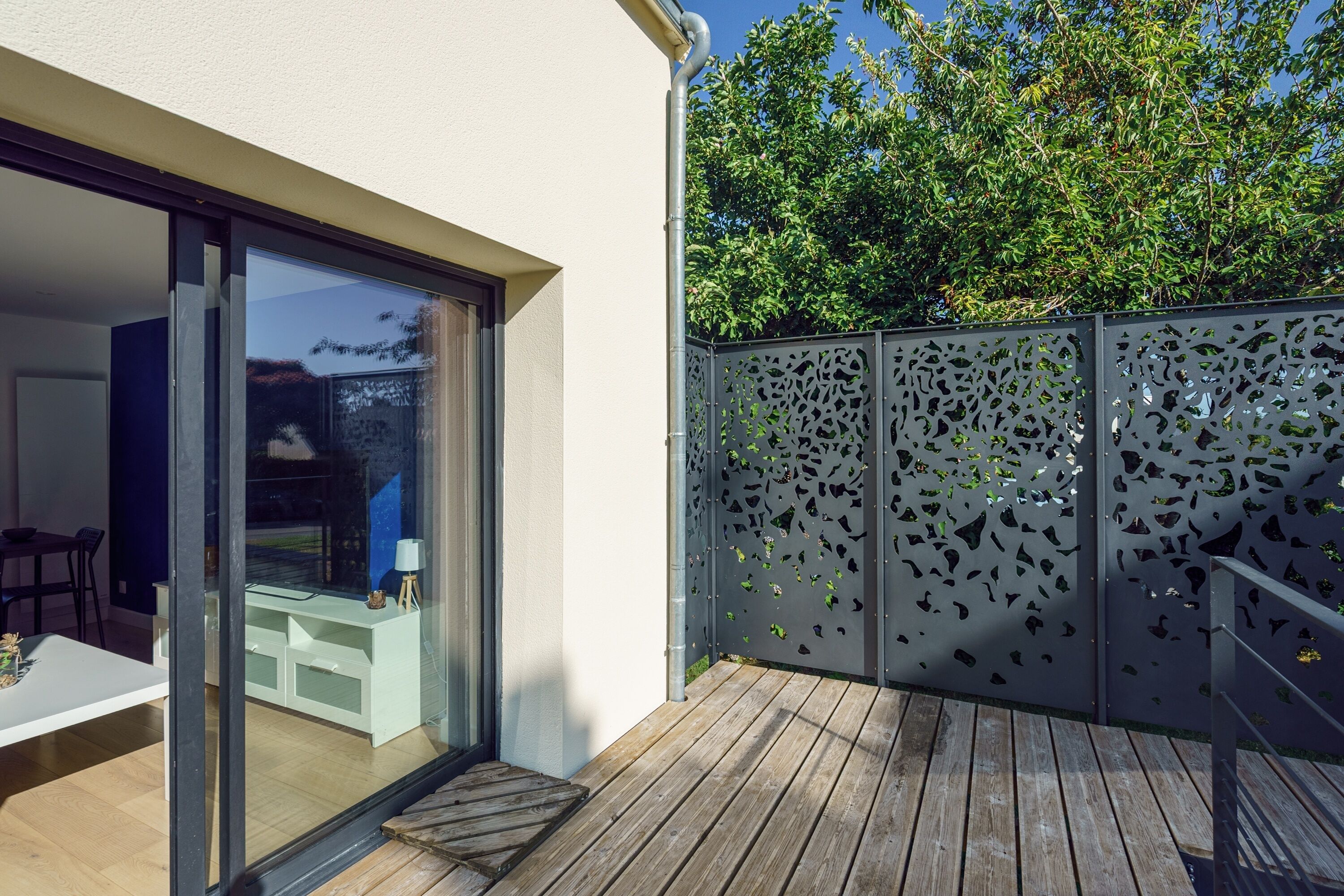 A modern outdoor deck with a wooden floor and a glass door leading to a dining area.