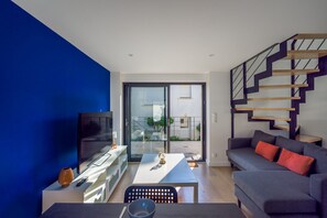 A modern living room with a blue accent wall, a staircase, a flat-screen TV, a sofa, and a dining area. - Ty Ker Briec - À 15 min de Quimper (Briec)