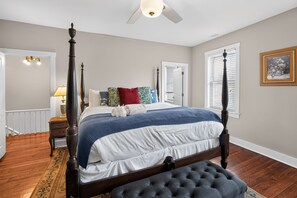 A bedroom with a four-poster bed, a tufted bench, a nightstand, a lamp, and a framed picture on the wall. - Change of Place Unit B - Victorian District (Savannah)