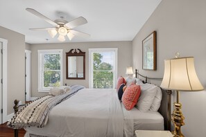 Ein Schlafzimmer mit Bett, Deckenventilator, Nachttisch, Lampe und einem Fenster mit Jalousien.