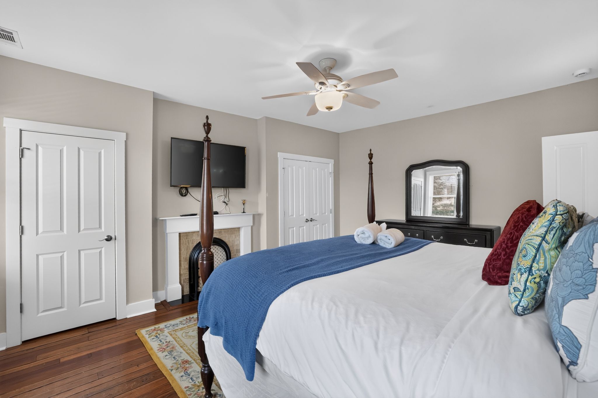 A bedroom with a bed, a ceiling fan, a television, a dresser, and a mirror.